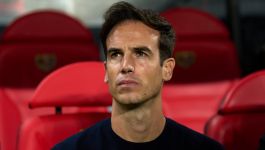 Na zdjęciu widzimy trenera Rayo Vallecano, Íñigo Péreza, siedzącego na ławce rezerwowych stadionu piłkarskiego. W tle znajdują się charakterystyczne czerwone fotele, typowe dla trybun dla sztabu szkoleniowego. Íñigo Pérez ubrany jest w ciemny sweter i koncentruje się, prawdopodobnie obserwując przebieg spotkania lub przygotowując się do meczu swojej drużyny. Fotografia dobrze oddaje atmosferę przed ważnym pojedynkiem Rayo Vallecano w Lidze Konferencji z Lechem Poznań. 