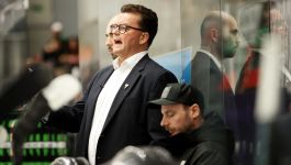 Pekka Tirkkonen, trener reprezentacji Polski (fot. PAP). Trener Pekka Tirkkonen podczas meczu hokejowego, ubrany w biały garnitur i okulary, wyraźnie emocjonuje się wydarzeniami na lodzie. Obok niego siedzi członek sztabu w czarnej kurtce i czapce z daszkiem. W tle odbicie obu mężczyzn w szklanej ścianie lodowiska. Tirkkonen komentuje minimalną przegraną GKS Tychy 4:5 w Lidze Mistrzów z fińskim Lukko, podkreślając dumę z zespołu i doświadczenia zdobyte na tle europejskiej czołówki(fot. PAP).